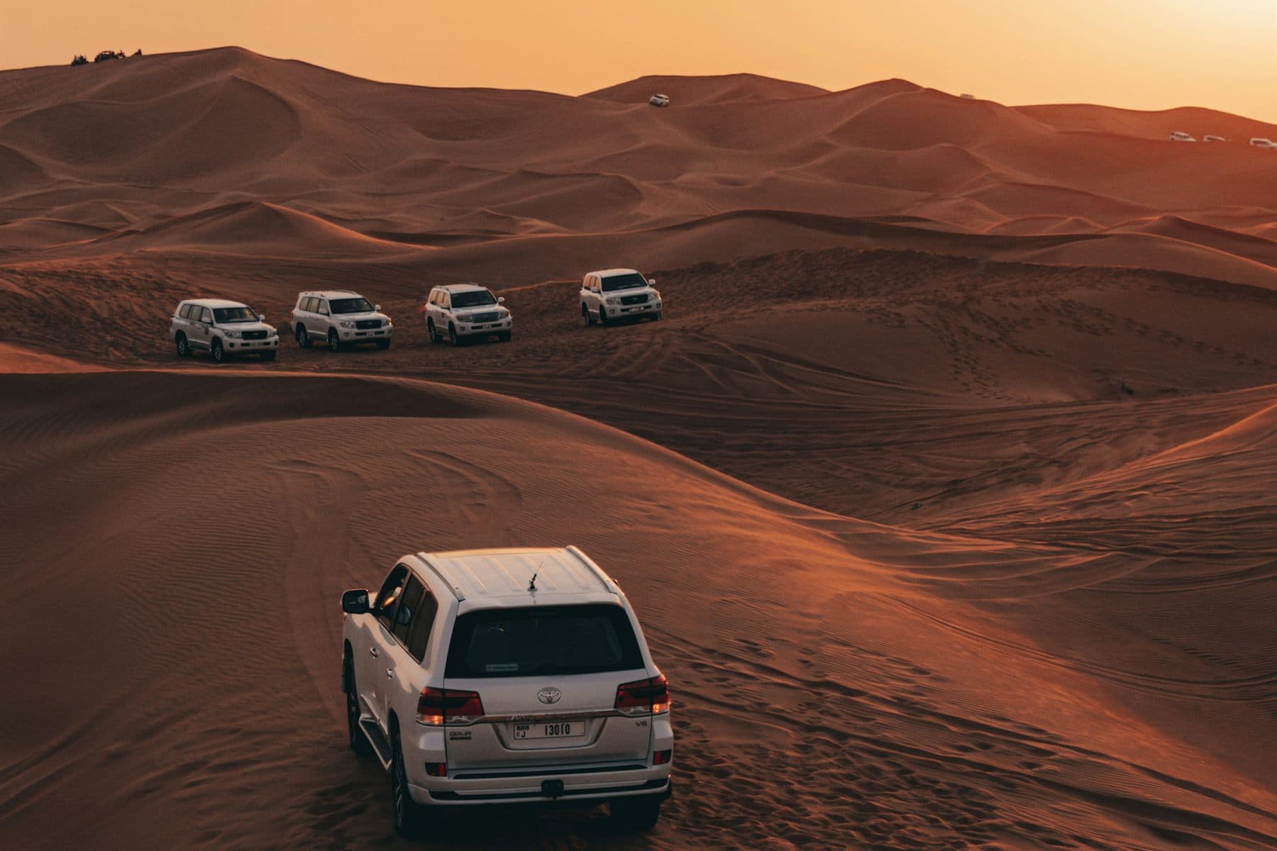 A convoy of white 4x4s crossing the dunes outside Dubai at sunset