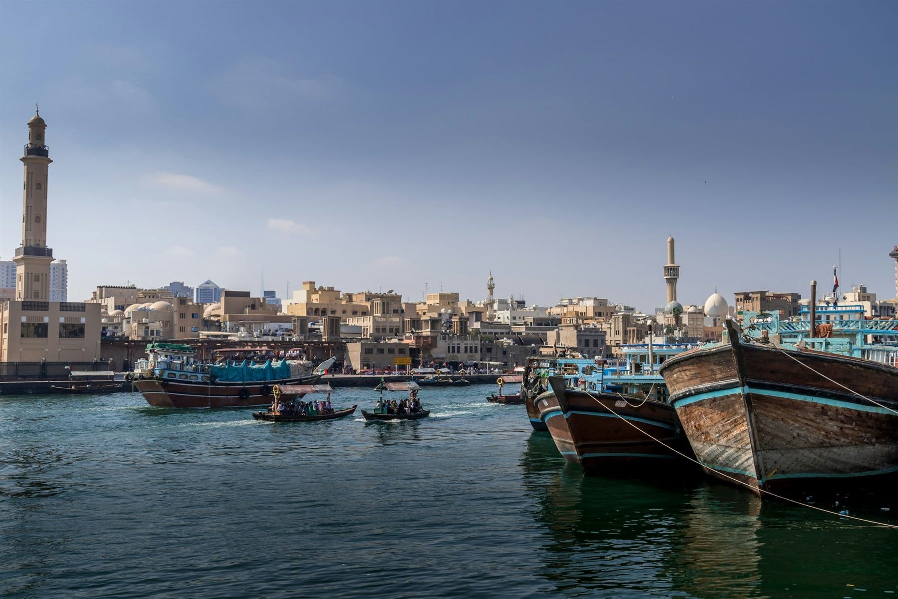 Abras and wooden dhows on Dubai Creek, with a mosque minaret above the old town
